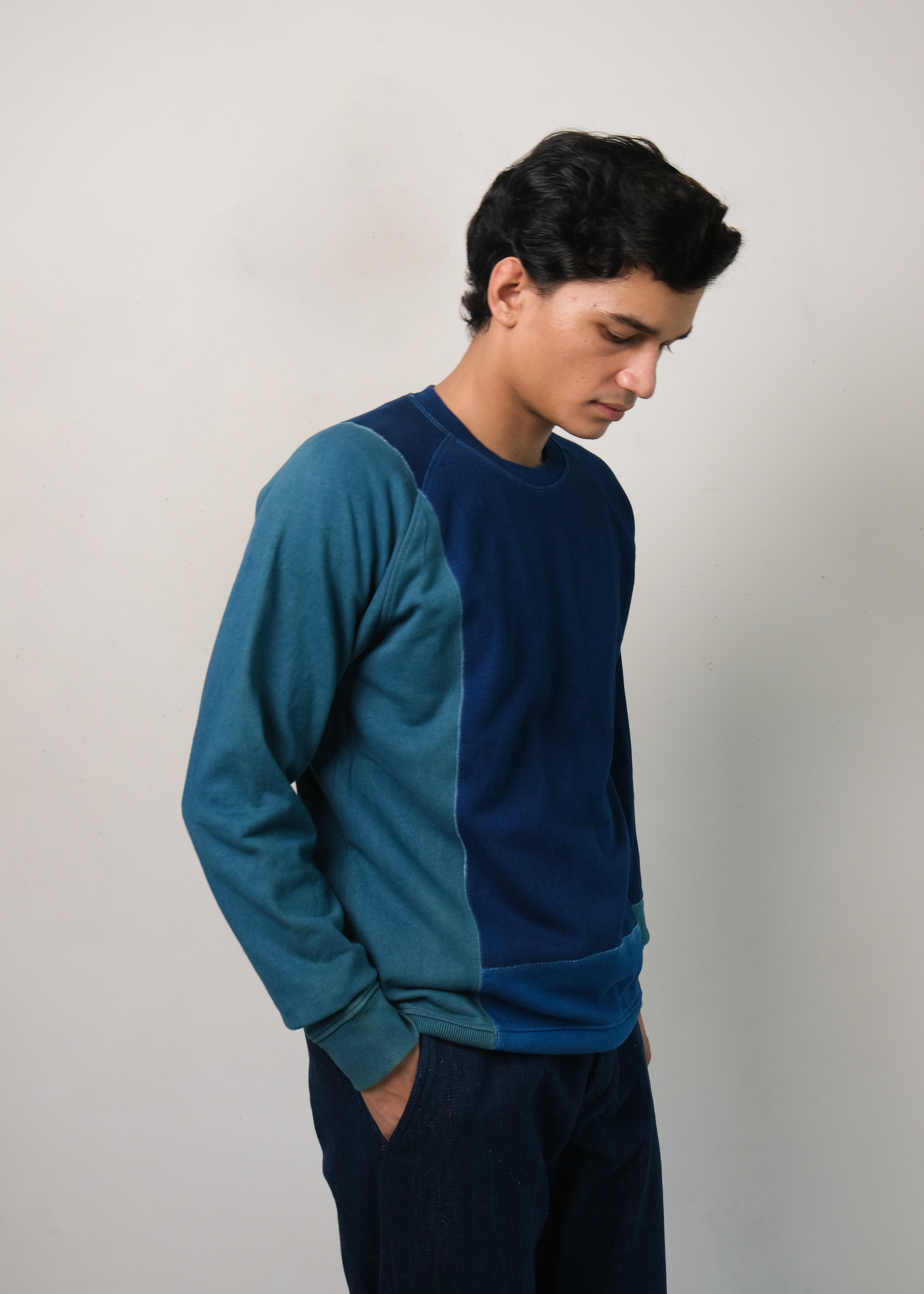 Man wearing a indigo and patchwork sweatshirt against a plain background