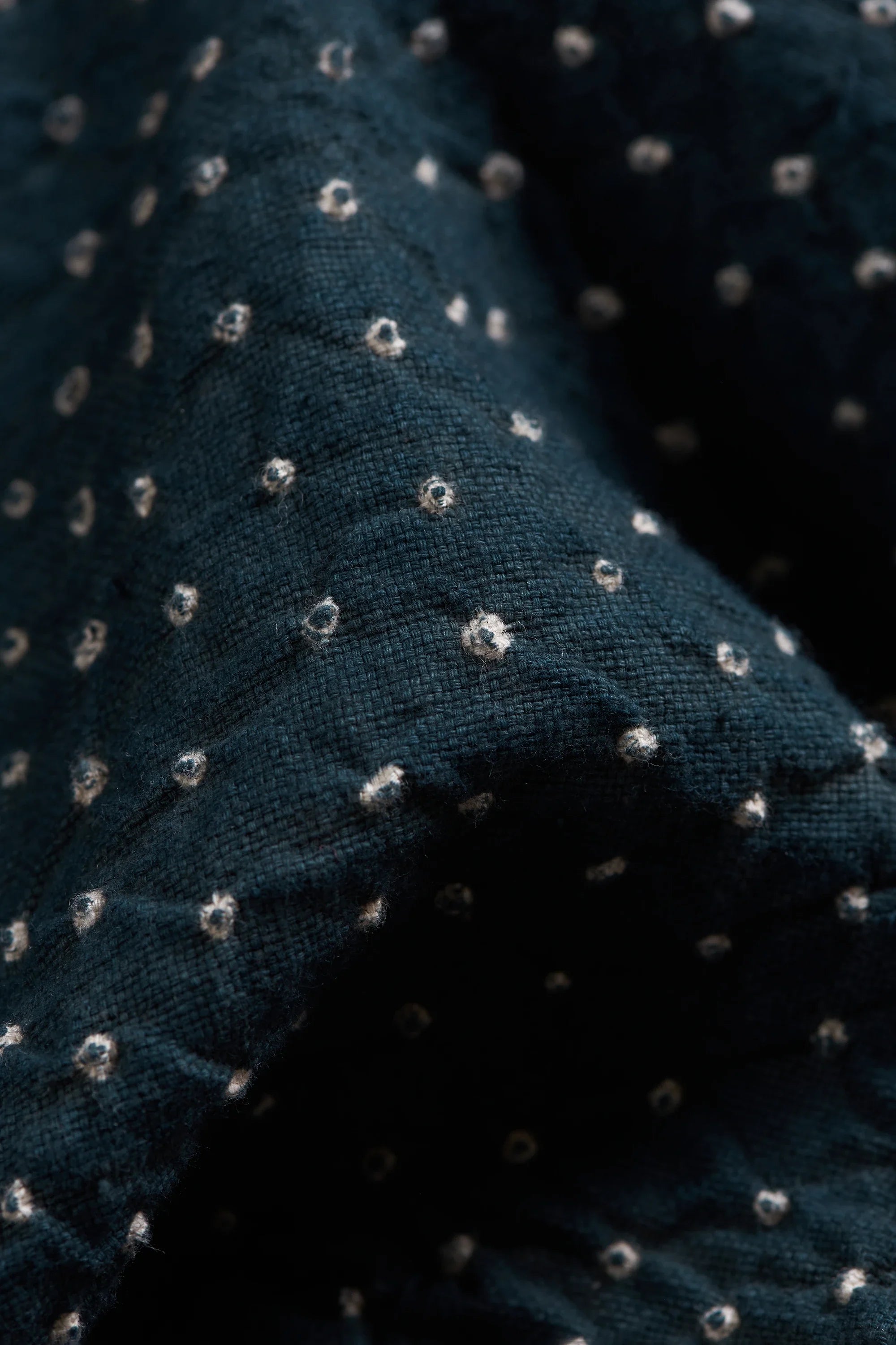 Close-up of fabric with a small white bandhani dot pattern, showing the texture and folds of the material.