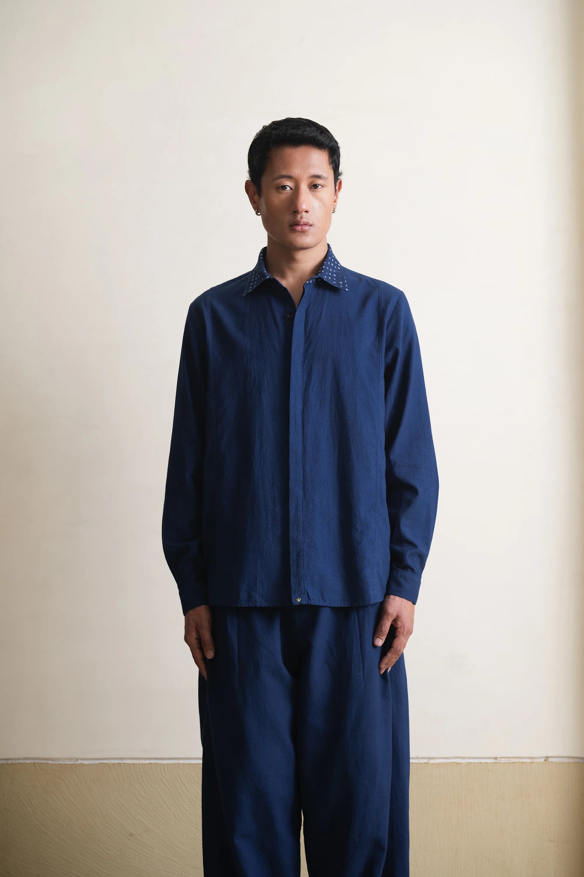 Man wearing a blue shirt and pants against a plain background