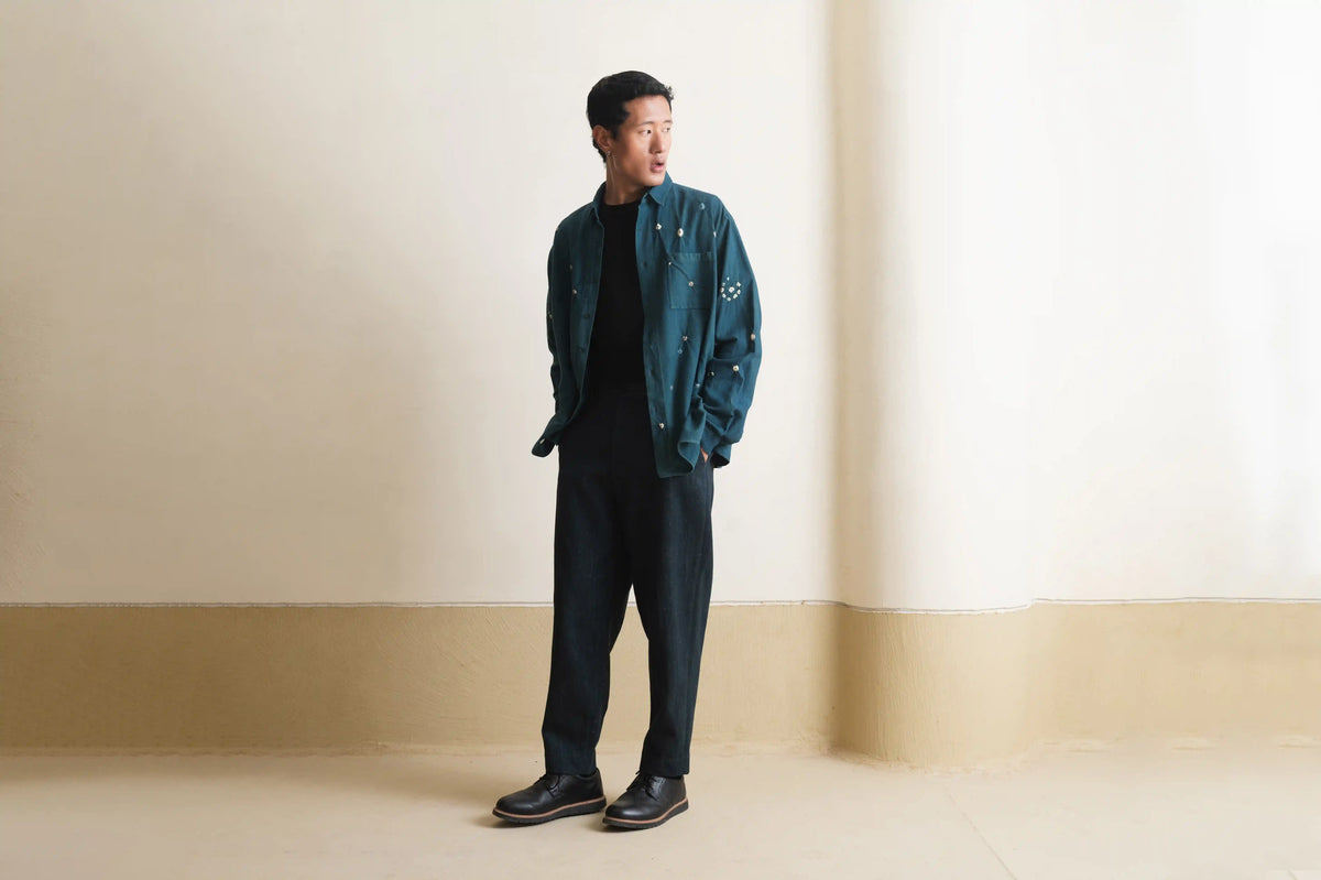 Man wearing a bottle green jacket over a black shirt and pants against a light grey wall