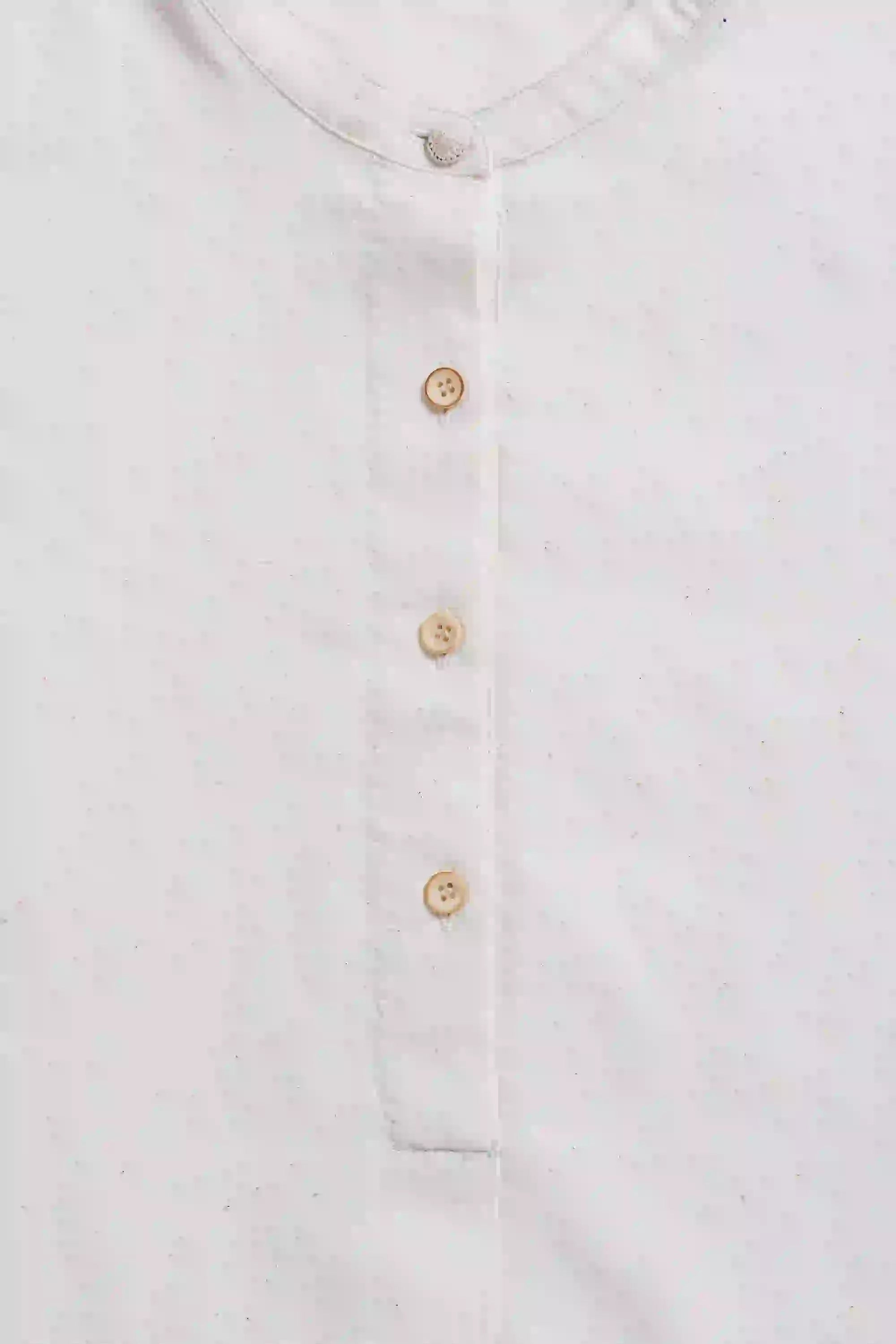 Close-up of a ecru shirt with gold buttons on a grey background