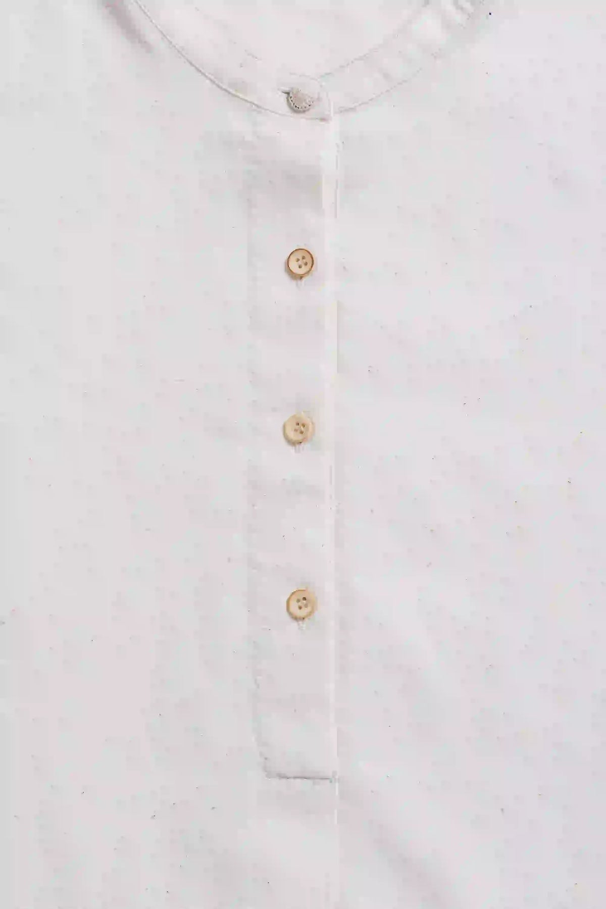 Close-up of a white shirt with gold buttons on a light gray background