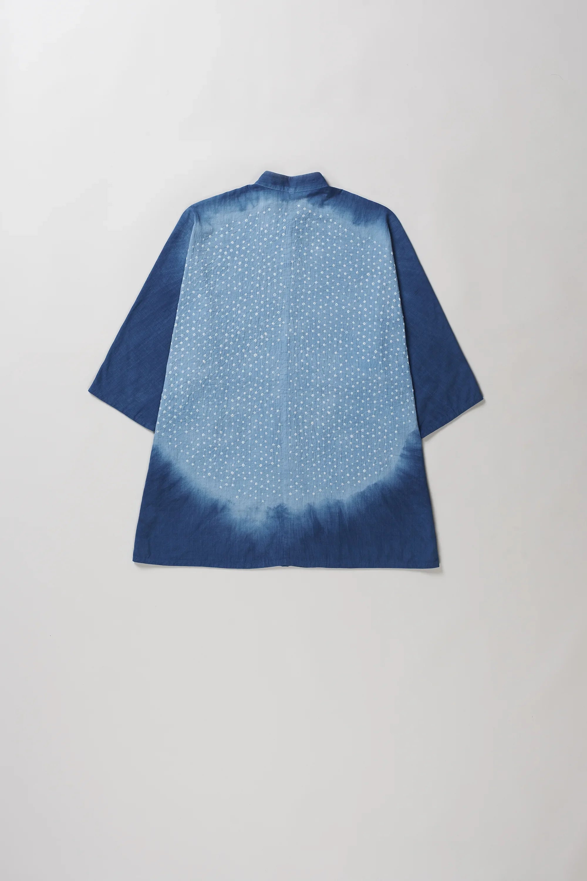 A medium indigo and tie-dye short-sleeve shirt shown from the back, featuring a solid dark blue border and a lighter blue center with a white dotted pattern.