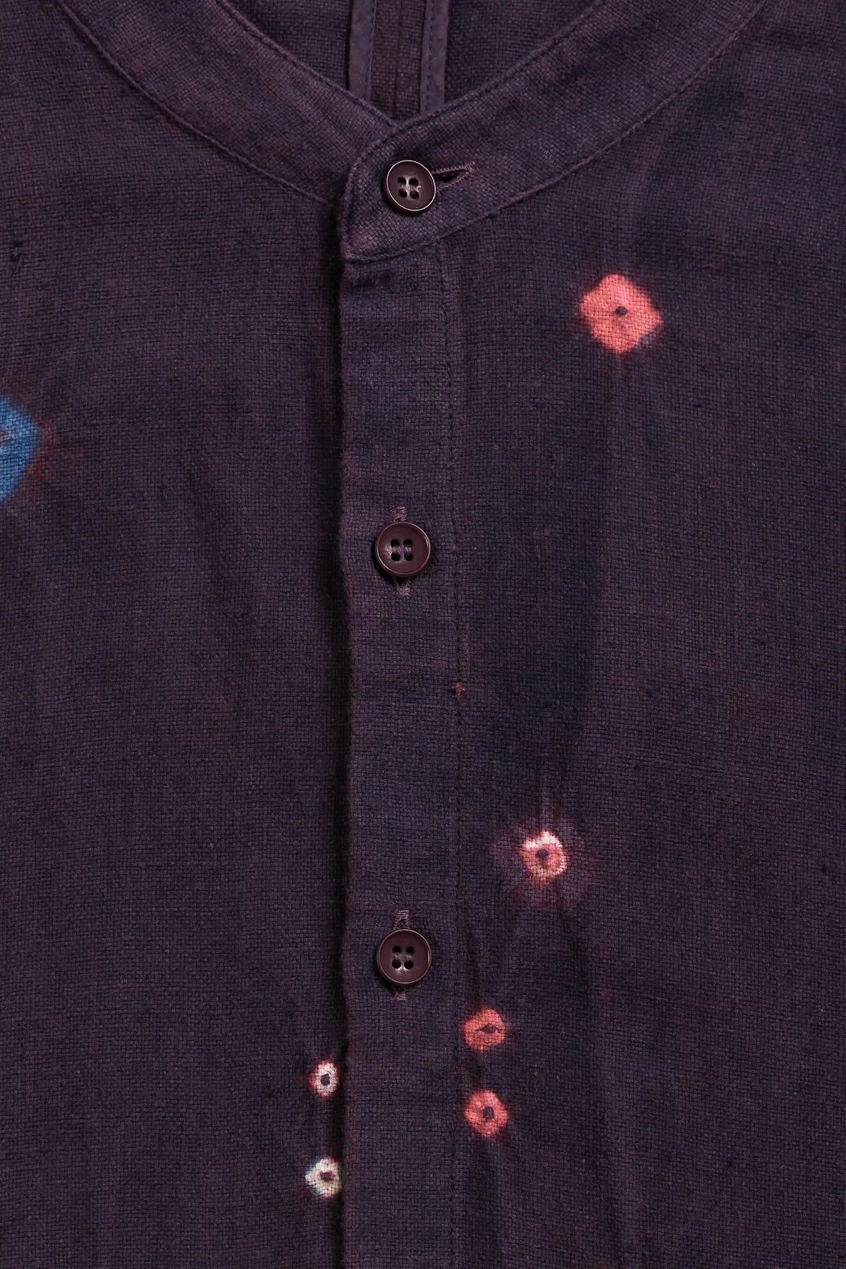 Close-up of a purple red button-up shirt with small pink and white tie-dye style flower motifs on the fabric.