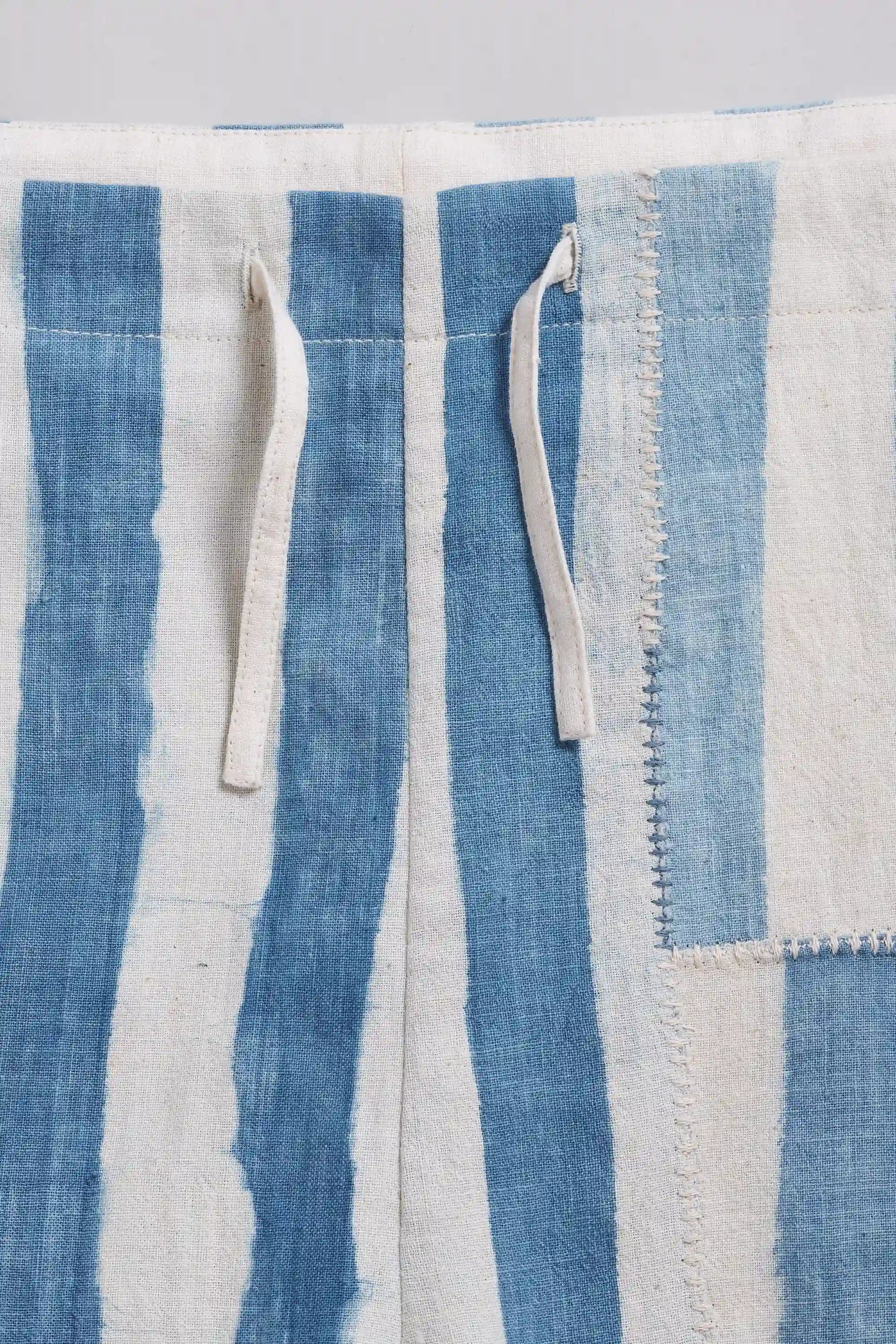 A close-up of a blue and off-white striped fabric with visible texture, two drawstring ties, and a stitched border detail.
