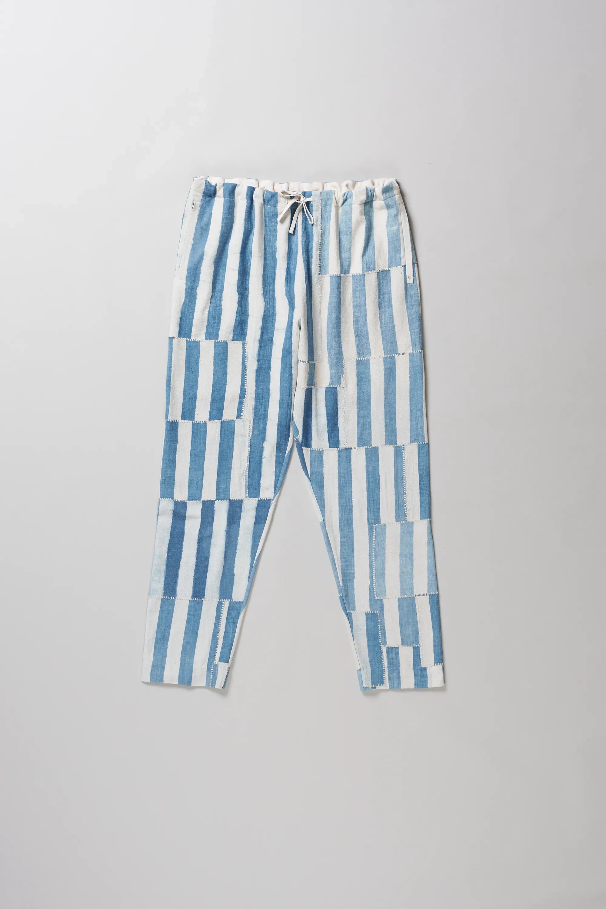 Light indigo and white vertically striped cropped pants with a drawstring waist, laid flat on a light grey background.