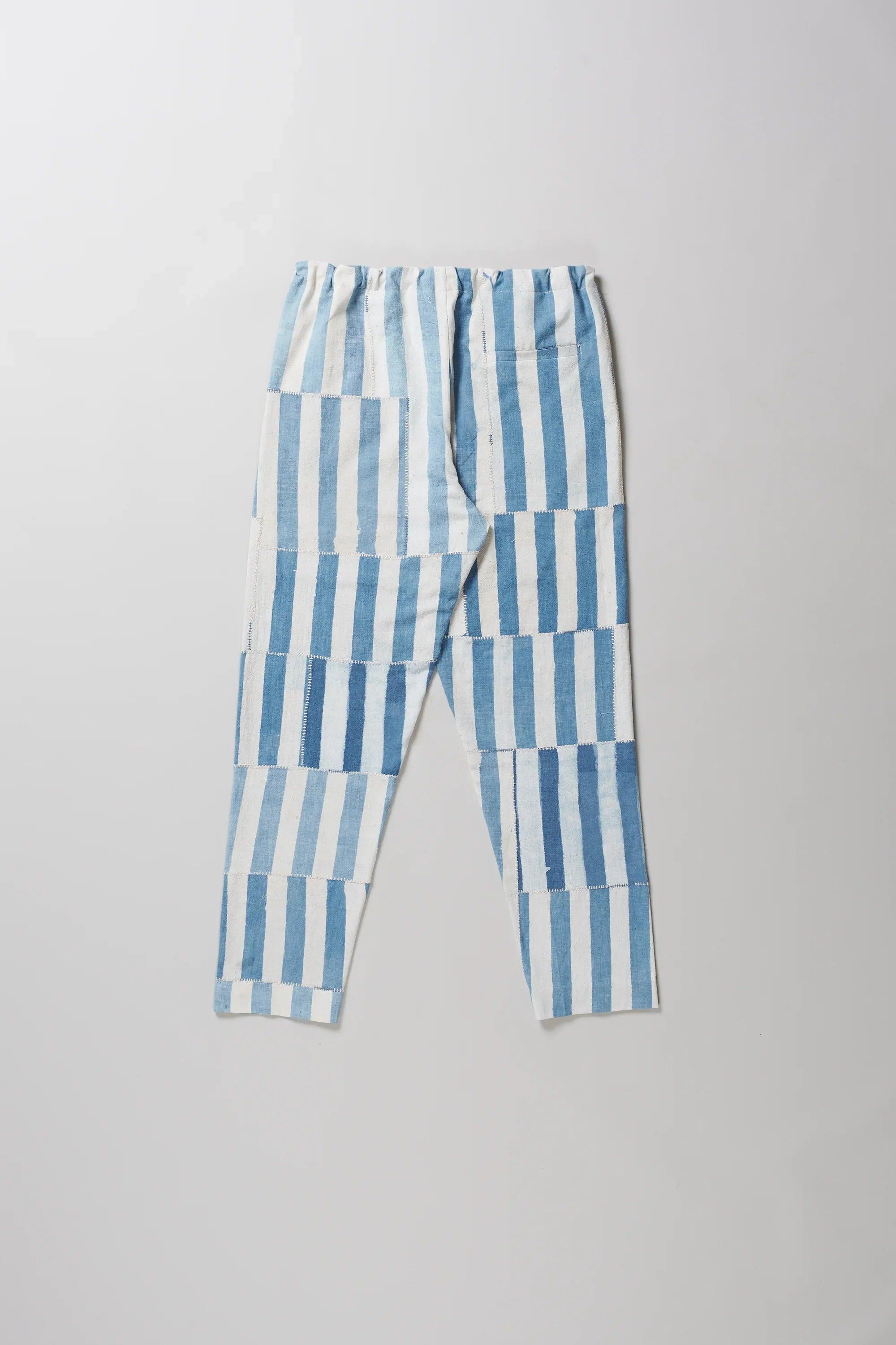 Back light indigo and white vertically striped cropped pants with a drawstring waist, laid flat on a light grey background.