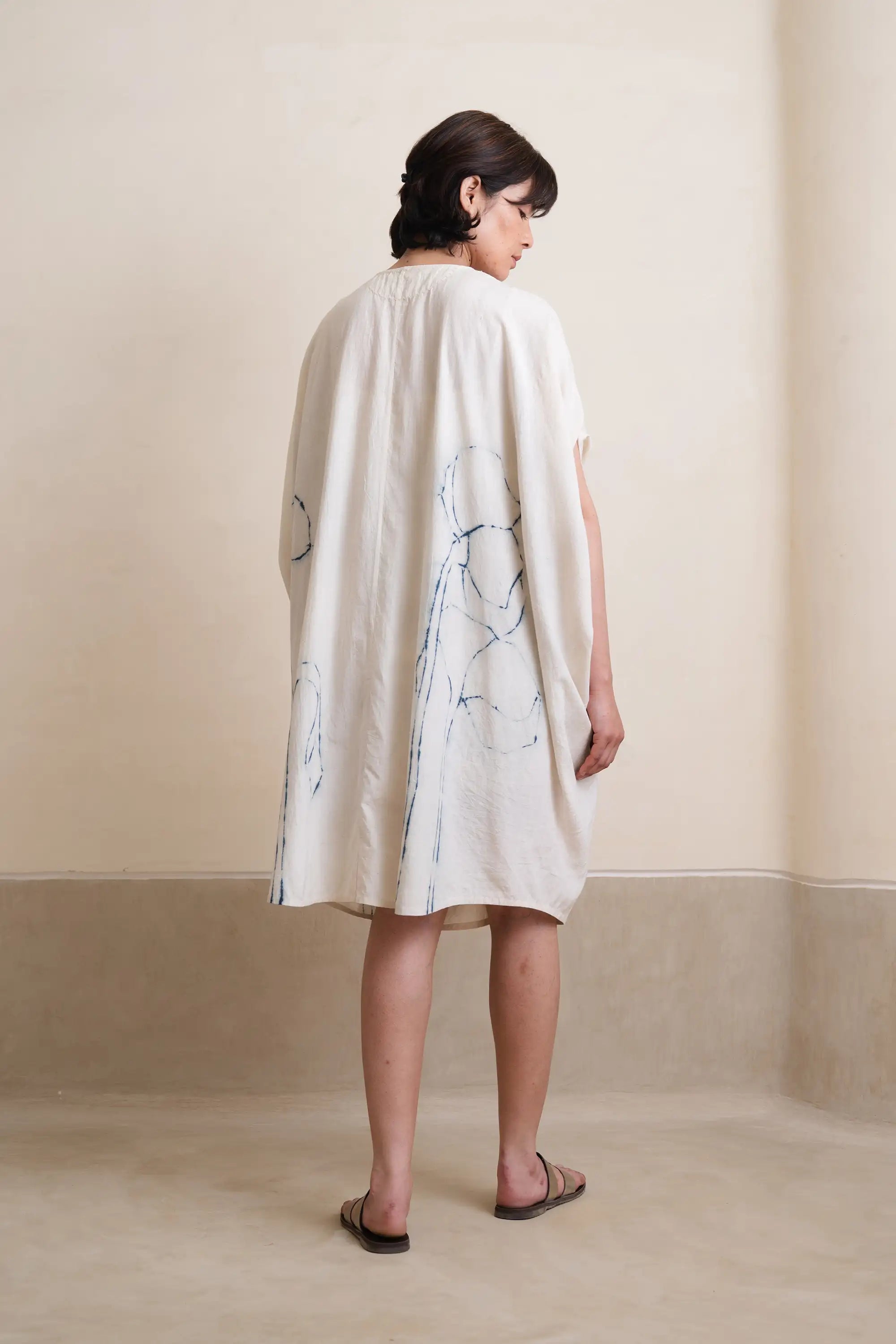 Woman wearing a light-colored dress with abstract patterns against a plain background